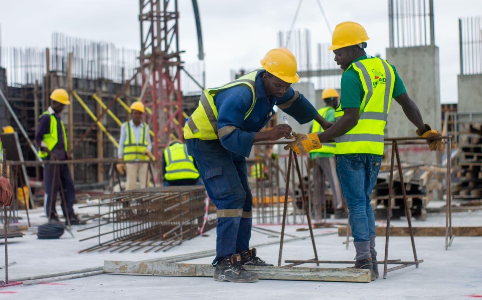 Two construction workers in high-visibility vests tying steel reinforcement on a building site