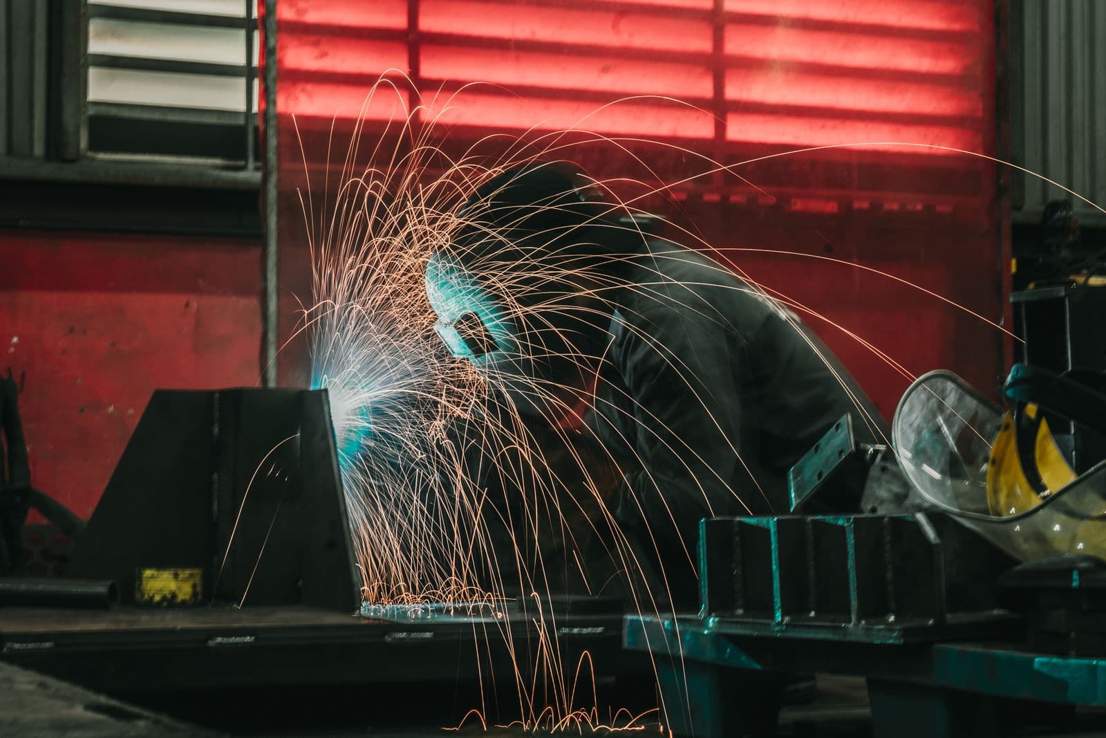 Welder working on steel fabrication, sparks arcing across a workshop