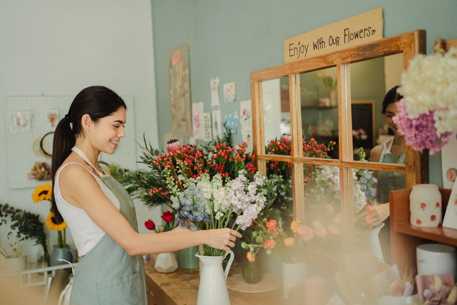 Florist in an apron arranging fresh flowers into a jug in a bright flower shop