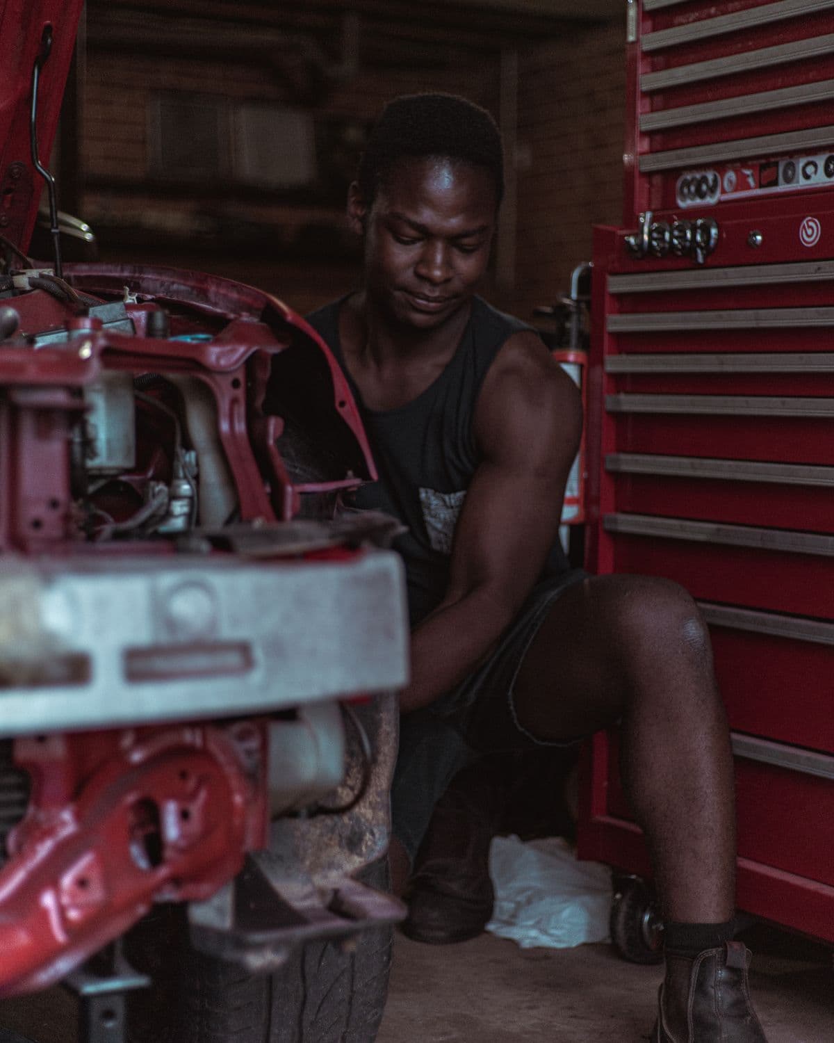 Mechanic crouched beside a partly stripped car in a workshop, tool chest behind him