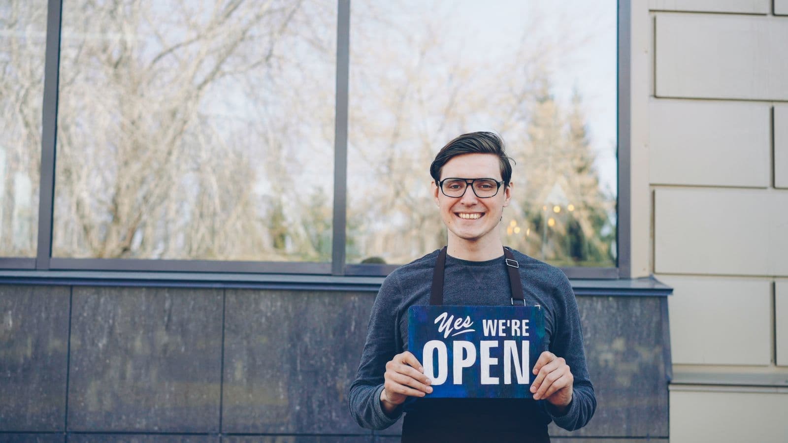 Shop owner in an apron holding an open sign outside their business