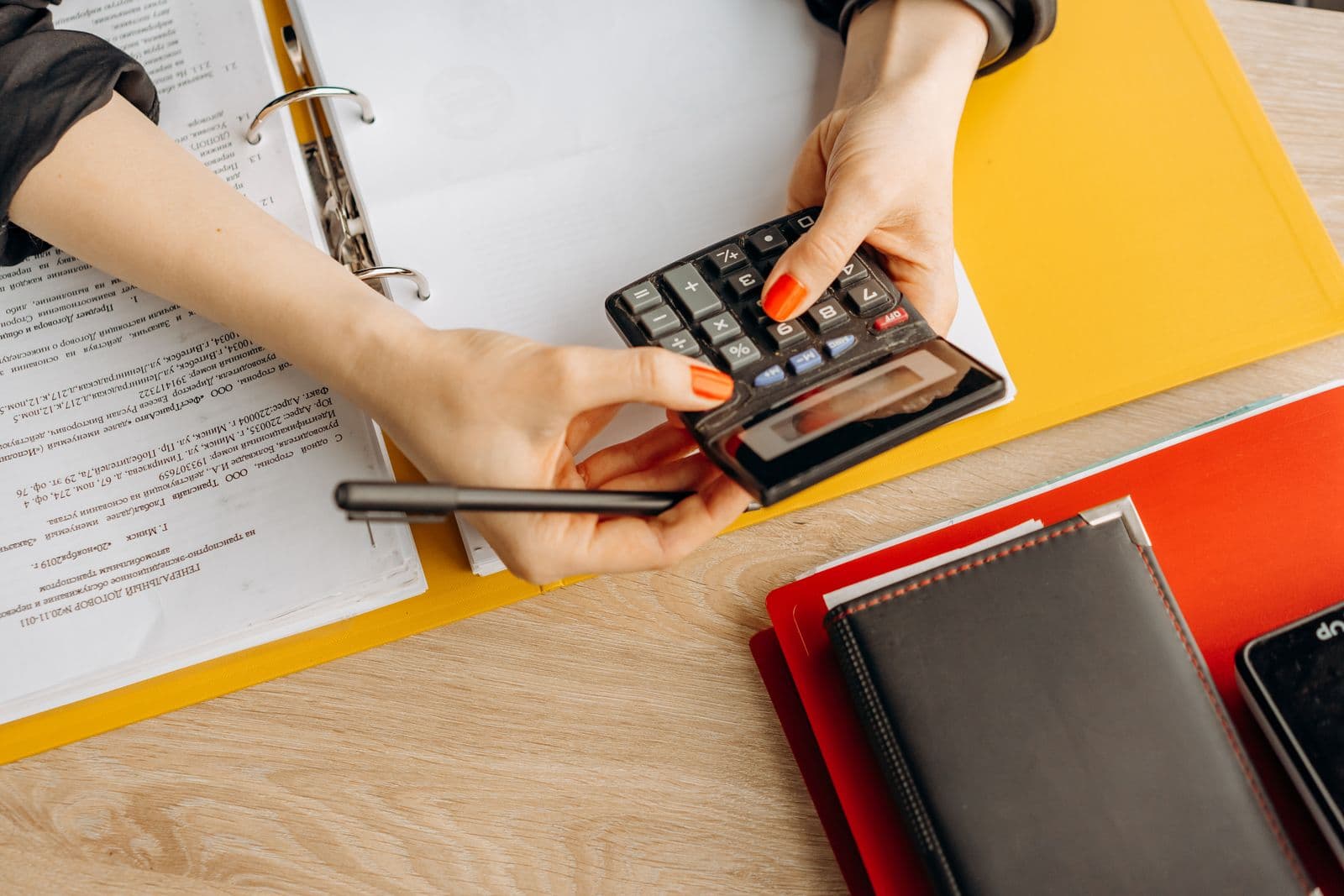 Hands using a calculator beside a ring binder and coloured folders of paperwork
