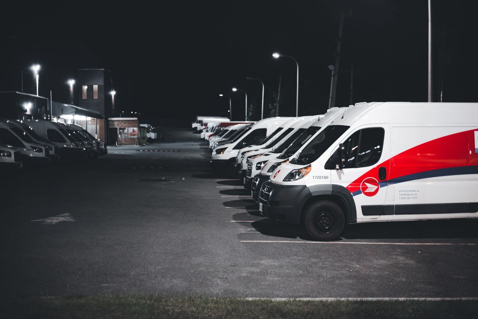 A row of commercial delivery vans parked under lights at night