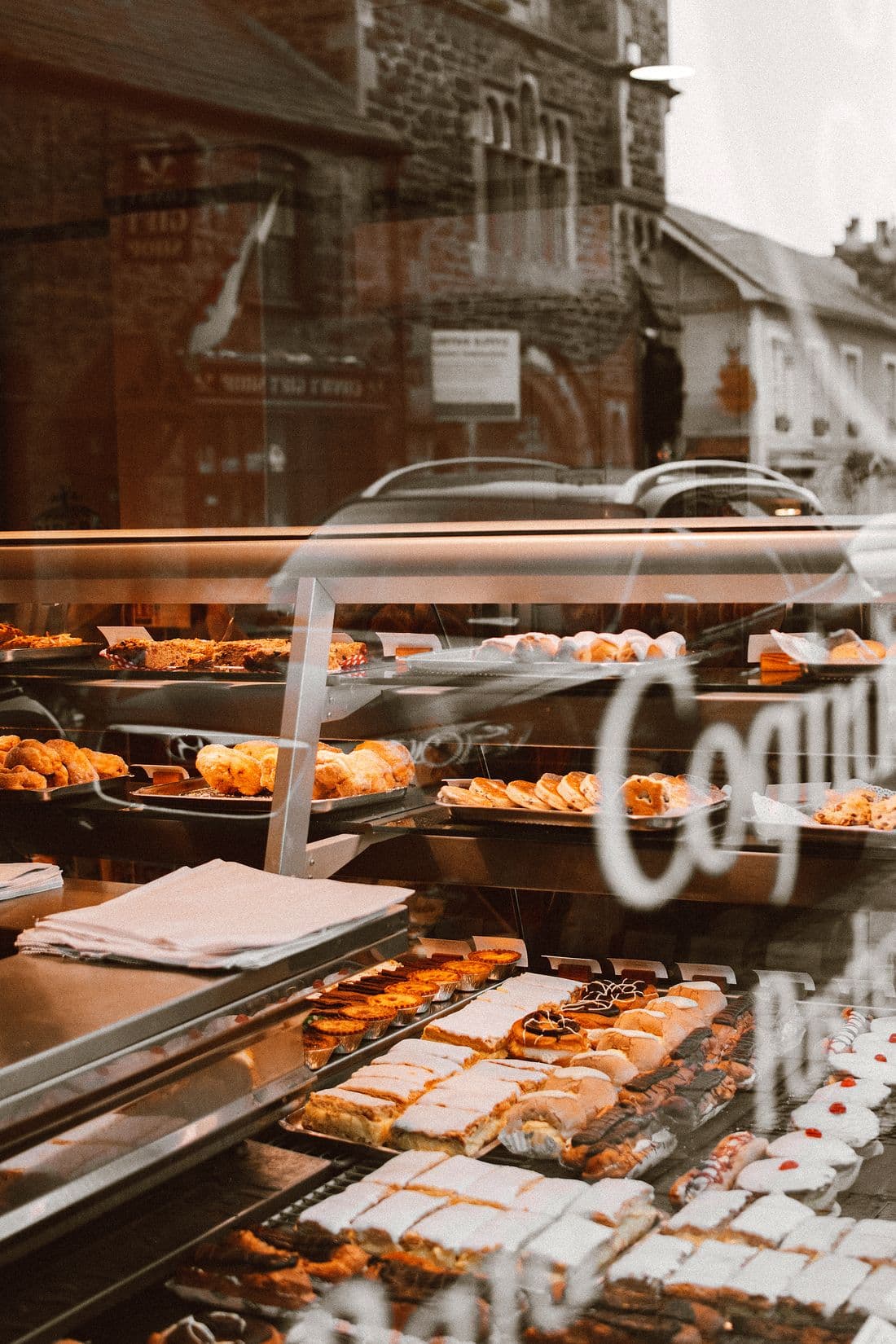 Trays of pastries and bread in a bakery window, seen through lettered glass